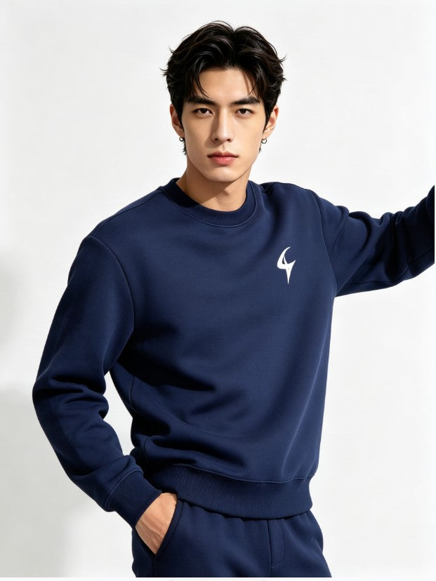 A man wearing a navy blue sweatshirt and matching sweatpants set, featuring a small white stylized logo on the left chest, posed against a clean white studio background.