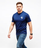 A man wearing a navy blue athletic t-shirt with a white lightning bolt logo on the left chest, paired with blue jeans, photographed against a solid white background.