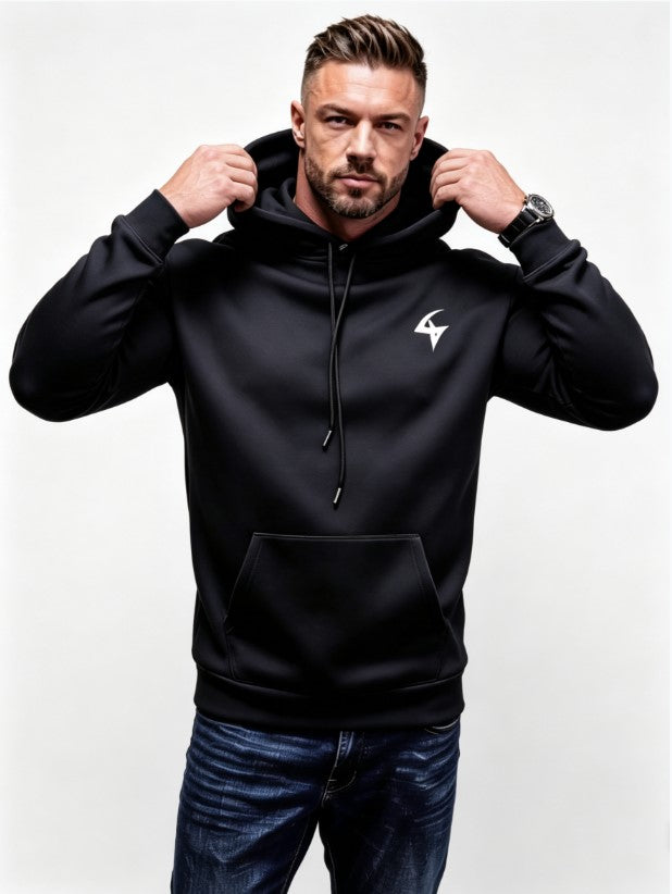 A man wearing a black pullover hoodie with a white stylized logo on the left chest, posing with his hands on the hood drawstrings against a light gray background.