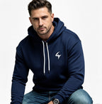 A man wearing a navy blue pullover hoodie with white drawstrings and a white stylized logo on the left chest, paired with blue jeans, set against a plain white background.
