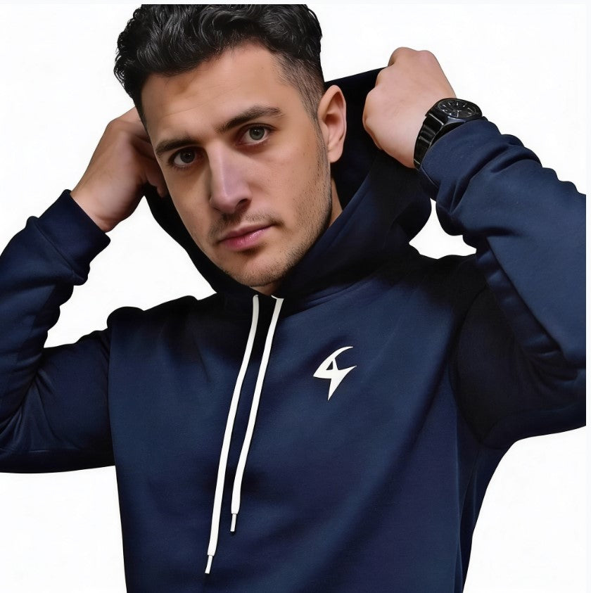 A man wearing a navy blue pullover hoodie with white drawstrings and a white lightning-bolt logo on the left chest, posing with his hands in his hoodie hood against a plain white background.