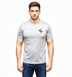 A man wearing a light gray short-sleeve athletic t-shirt with a black stylized logo on the left chest, paired with blue jeans, against a plain white background.