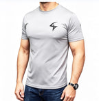 A man wearing a light gray short-sleeve athletic t-shirt with a black lightning-bolt style logo on the left chest, paired with blue jeans against a plain white background.