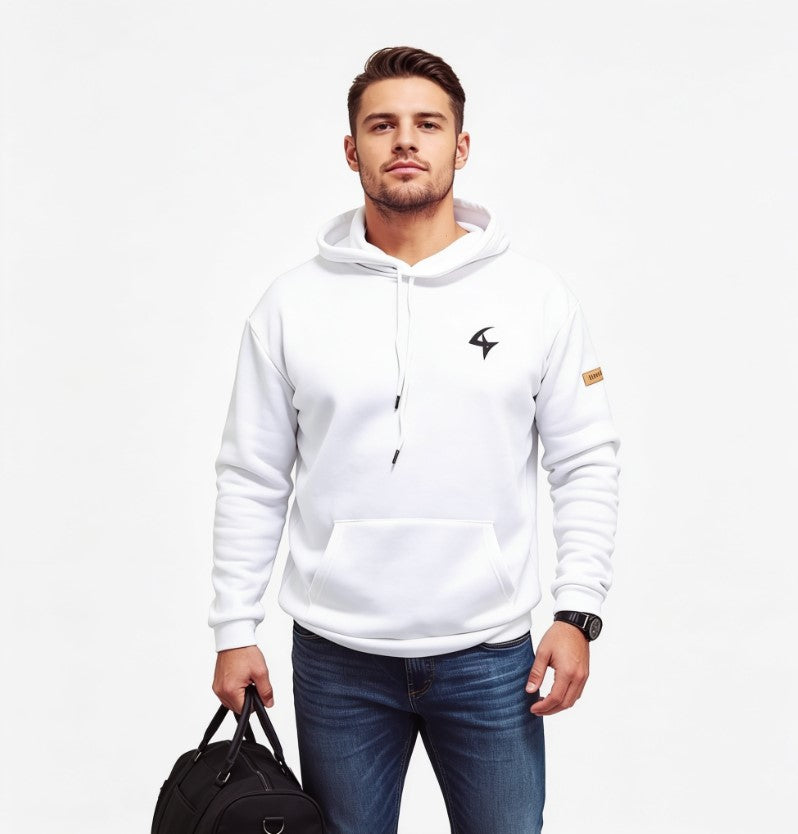 A man wearing a white pullover hoodie with a small black logo on the left chest and a small brown patch on the sleeve, paired with blue jeans, holding a black bag against a plain white background.