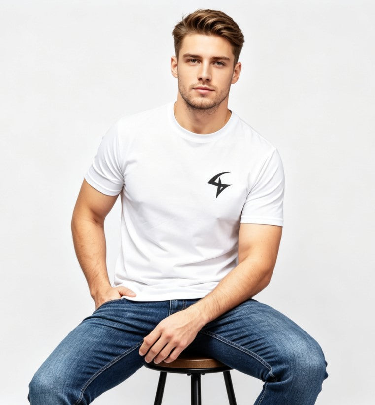 A man sitting on a stool wearing a white short-sleeve t-shirt with a black geometric logo on the left chest, paired with blue jeans, against a light gray studio background.