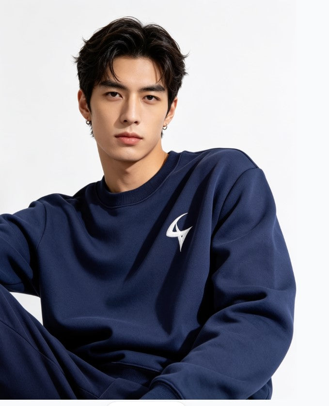 A man wearing a navy blue sweatshirt with a white stylized logo on the left chest, posed against a clean white studio background.